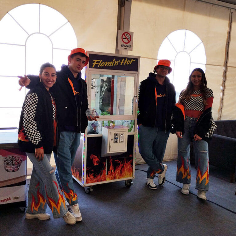 Equipo promocional con ropa Flamin Hot posando junto a la maquina atrapa peluches