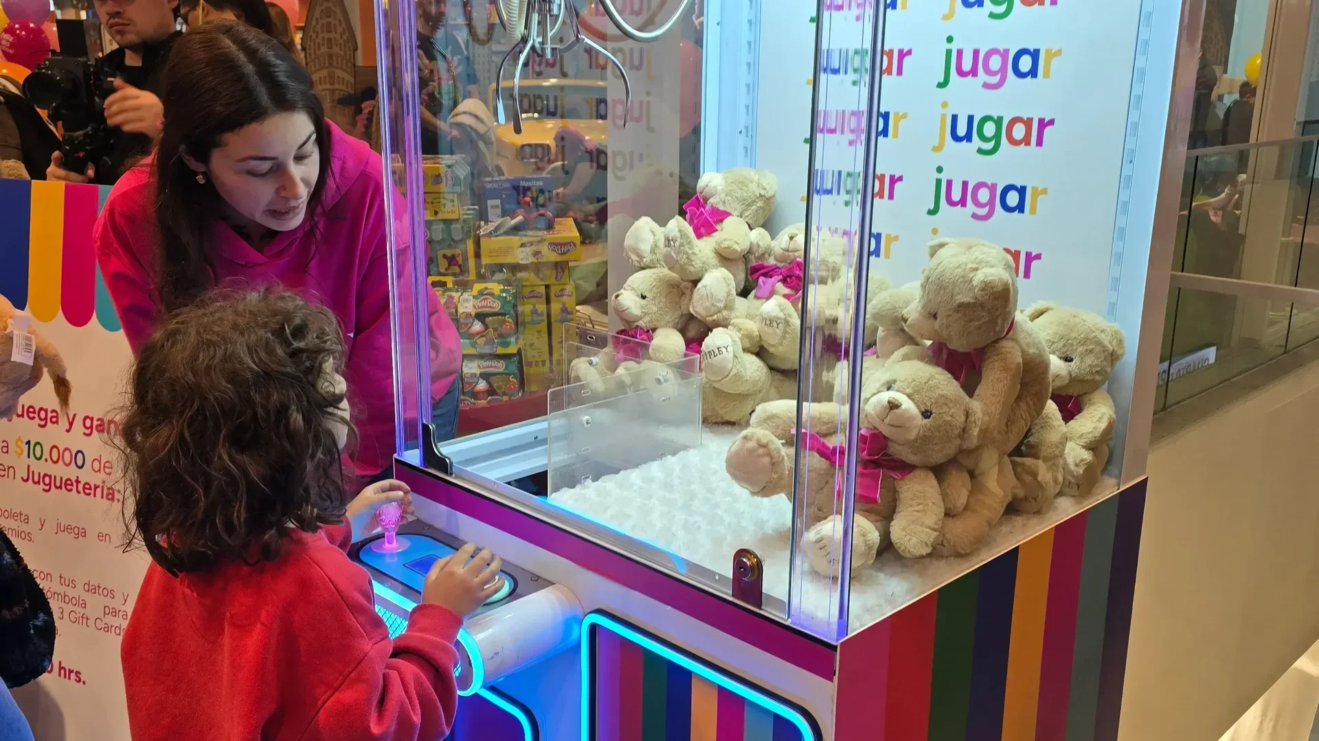 Niño manejando la palanca de una peluchera rosada llena de ositos de peluche durante una celebración infantil
