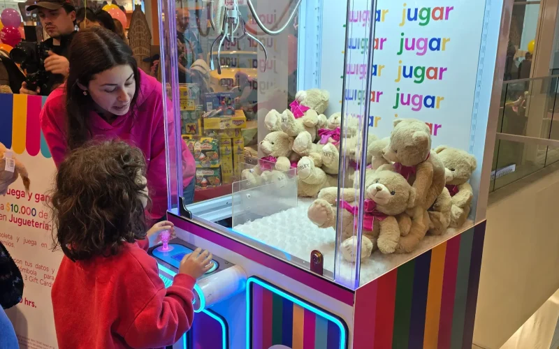 Niño manejando la palanca de una peluchera rosada llena de ositos de peluche durante una celebración infantil