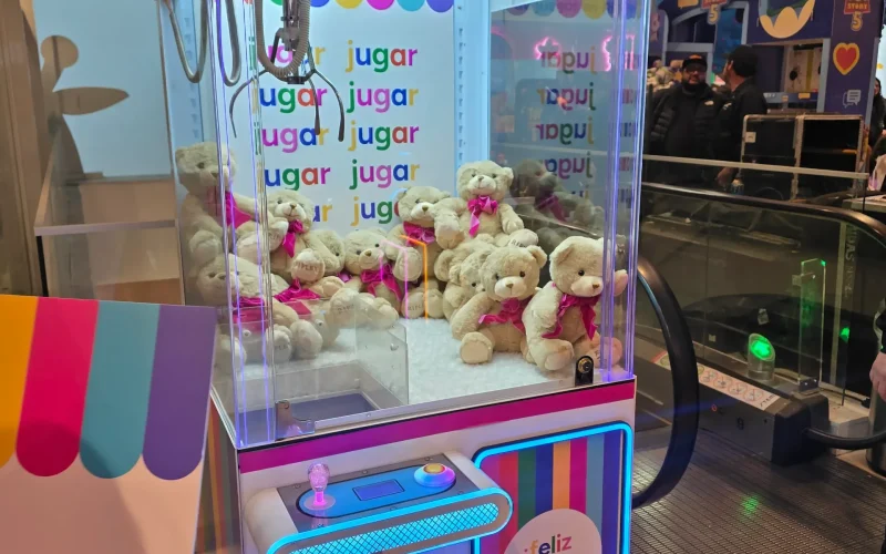 Máquina atrapa peluches rosada de Ripley llena de ositos de peluche con lazos, iluminada con neón en un mall